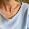 Woman wearing two gold necklaces including a Rosecliff bar necklace with eleven alternating 2 mm alexandrites and diamonds