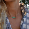 Woman wearing a Rosecliff bar necklace with eleven 2 mm faceted round cut emeralds prong set in solid 14k yellow gold