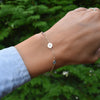 Woman's hand with a 14k gold Classic bracelet featuring two birthstones and one 1/4” flat disc engraved with the letter H