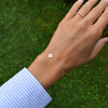 Woman's hand with a 14k gold Classic bracelet featuring one white topaz and one 1/4” flat disc engraved with the letter H