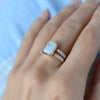 Woman's hand wearing a Warren ring in 14k gold with accent diamonds featuring one 10 x 8 mm emerald cut rainbow moonstone