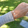 Woman wearing a 14k gold Classic bracelet featuring three 1/4” flat letter-engraved discs, spelling M-heart-M