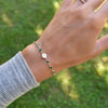 Woman wearing a Newport 14k gold bracelet featuring 4 mm briolette emeralds and a 1/4” flat disc engraved with the letter H