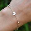 Woman with a 14k yellow gold Classic bracelet featuring birthstones and 1/4” flat letter-engraved discs