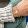 Woman with three bracelets including a 14k gold Noel bracelet featuring one 1/4” flat disc engraved with a snowflake