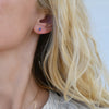 Close-up of a woman's ear wearing a Providence Sapphire stud earring with a petite baguette stone set in 14k yellow gold