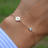 Woman wearing a 14k gold Classic bracelet featuring one Nantucket blue topaz & one 1/4” flat disc engraved with the letter H