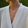 Woman wearing two necklaces including a 14k gold necklace featuring three 1/4” flat engraved letter discs, spelling Mom
