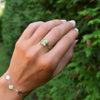 Woman wearing a Greenwich ring featuring four 4 mm faceted round cut peridots and one 2.1 mm diamond prong set in 14k gold