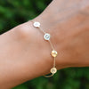 Woman's hand with a 14k yellow gold bracelet featuring four 1/4” flat letter-engraved discs, spelling VOTE