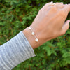 Woman's hand wearing a 14k yellow gold cable chain bracelet featuring three 1/4” flat engraved letter discs, spelling MOM