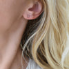 A woman's ear wearing a Providence Pink Tourmaline stud earring with a petite baguette stone set in 14k yellow gold