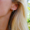 Woman wearing a Rosecliff huggie earring featuring nine alternating 2 mm emeralds & diamonds prong set in 14k yellow gold