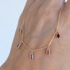 A woman's hand holding a Providence 5 Ruby drop necklace featuring 5 petite baguette cut stones set in 14k yellow gold