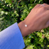 Woman wearing a 14k yellow gold cable chain bracelet featuring one 1/4” flat disc engraved with the letter Q