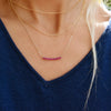 Woman wearing layered necklaces including a Rosecliff bar necklace with 2 mm faceted round cut rubies prong set in 14k gold