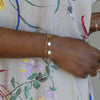 Woman wearing several bracelets including a 14k yellow gold cable chain bracelet featuring 1/4” flat engraved letter discs