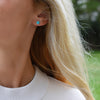 Woman wearing a 14k yellow gold Grand stud earring featuring one 6 mm briolette cut bezel set turquoise