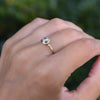 Woman's hand wearing a 1.6 mm wide 14k yellow gold Grand ring featuring one 6 mm briolette cut bezel set white topaz